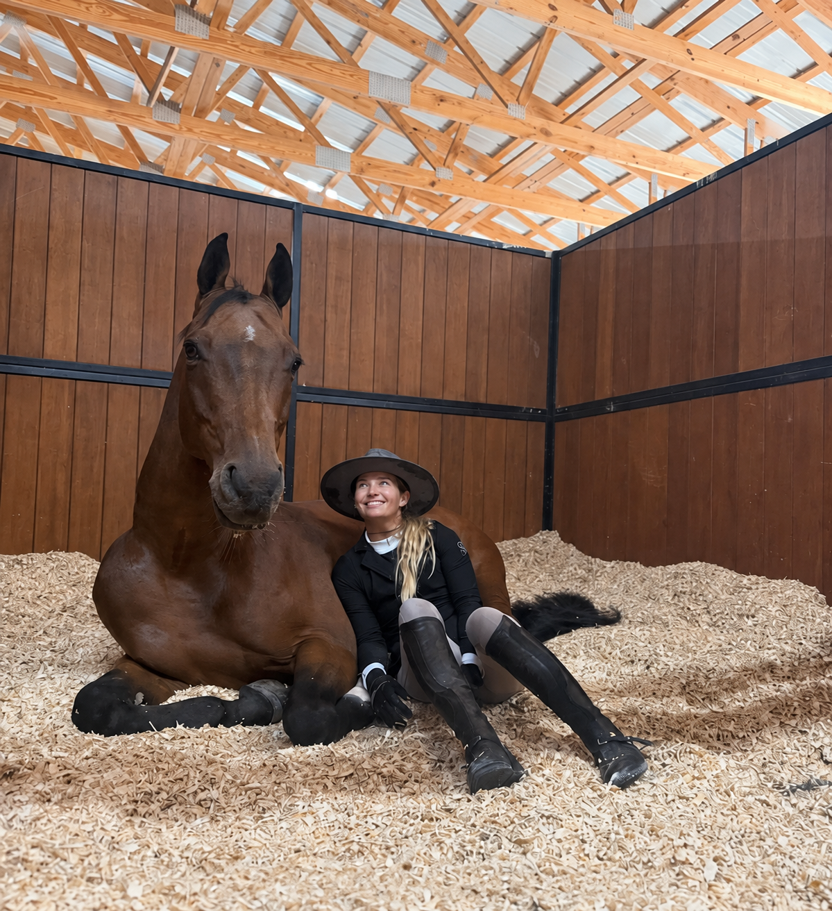 Ashlee seated beside her resting horse in the stall